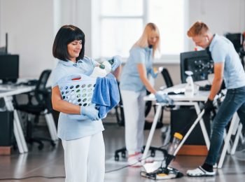 Woman with basket. Group of workers clean modern office together at daytime